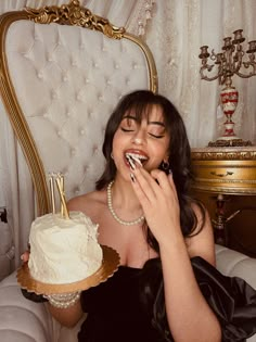 a woman sitting in a chair with a cake on her lap and one hand up to her mouth