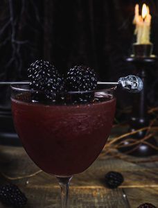 a glass filled with blackberries on top of a wooden table next to a candle