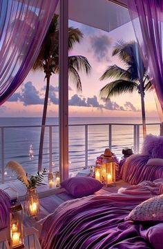 a bed with purple sheets and pillows next to the ocean