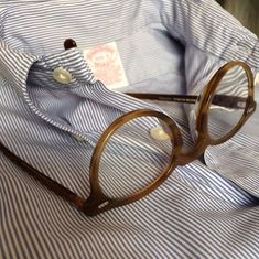 a pair of glasses sitting on top of a blue and white striped shirt with buttons