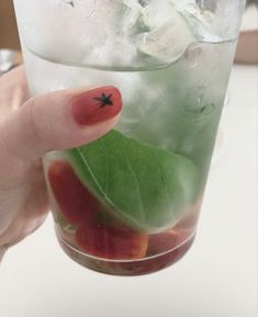 a person holding up a glass with ice and fruit in it, while wearing red fingernails