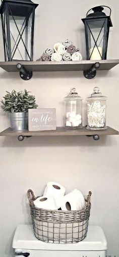 two shelves above a toilet with towels and baskets on top of it, along with candles