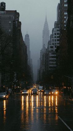 a city street at night with cars driving on the road and tall buildings in the background