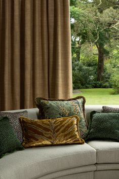 a couch with many pillows on top of it in front of a curtained window