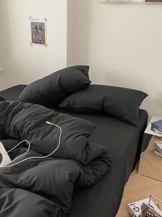 an unmade bed with black sheets and pillows on top of it in a bedroom