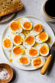 hard boiled eggs on a white plate next to bread and a cup of black coffee