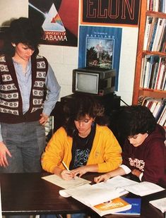 two young people are sitting at a table with books and papers in front of them