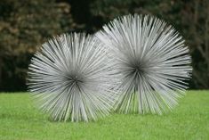 two metal sculptures sitting on top of a lush green field