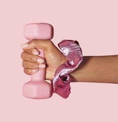 a woman's hand holding a pink object against a pink background with the top part of her arm wrapped around it