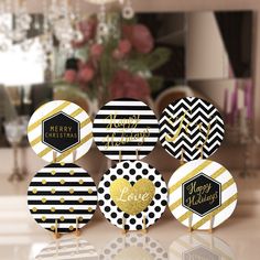 four black and white christmas decorations with gold foil lettering on them, sitting on a table