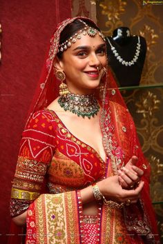 a woman in a red and gold bridal outfit with jewelry on her neck, smiling at the camera