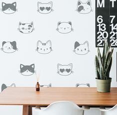 a wooden table topped with a potted plant next to a wall covered in cats