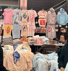 people are looking at shirts for sale in a market area with other items on display