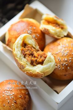 several rolls in a box with sesame seeds on the top and one bun filled with meat