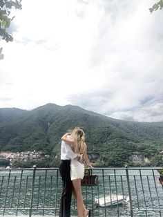 a man and woman standing on the edge of a pier next to a body of water