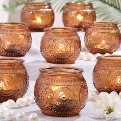 many gold colored candles are sitting on a table with flowers and pearls around them in front of a palm tree