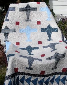 a quilted chair with an airplane pattern on it in front of some bushes and flowers