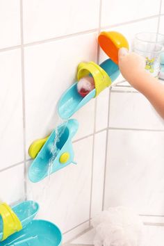 a child's hand is pouring water into a blue and yellow toothbrush holder