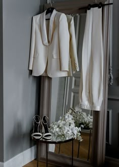 a white suit and shoes are on a table in front of a mirror with flowers