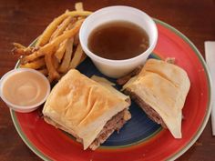 a plate topped with sandwiches and french fries next to dipping sauce on a wooden table