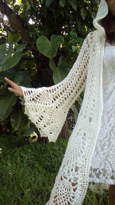 a woman wearing a white crochet shawl in the grass with her hand out