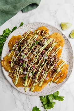 a white plate topped with meat and vegetables covered in green sauce next to cilantro