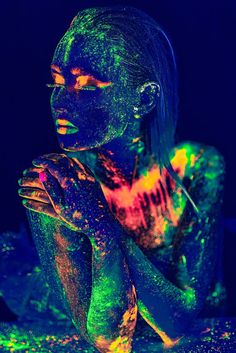 a woman is covered in neon paint and has her hands on her face while she looks at the camera