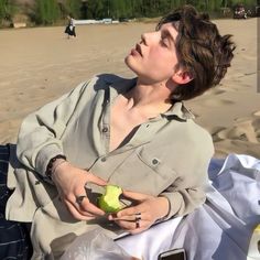 a woman sitting on the beach with an apple in her hand and looking up to the sky