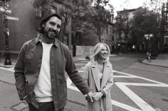 a man and woman holding hands while walking down the street in black and white photo