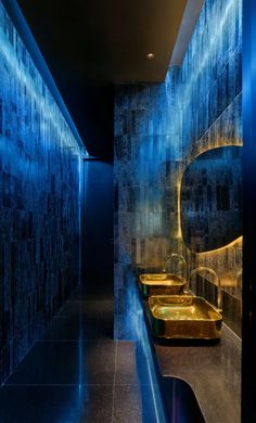 two sinks in a bathroom with blue lights on the wall and tiled walls behind them