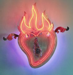 a heart shaped neon sign with flames and a piece of glass in the shape of a human head