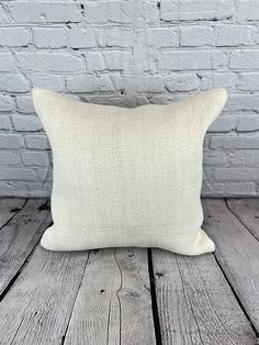 a white pillow sitting on top of a wooden table next to a brick wall and floor