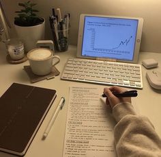 a person writing on a piece of paper in front of a laptop and coffee cup