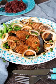 a plate with meat, onions and green beans on it next to some silverware