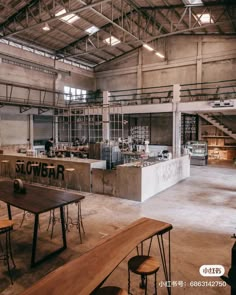 an industrial building with tables and benches in the foreground, open kitchen on the far side