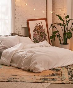 an unmade bed with white sheets and pillows in a room next to a potted plant