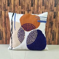 a decorative pillow with an orange, blue and white design on the front is sitting against a bamboo wall