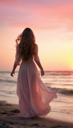 a woman walking on the beach at sunset with her hair blowing in the wind and wearing a flowing dress