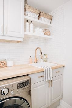 a washer and dryer in a small room with white cabinets, wood counter tops and open shelving