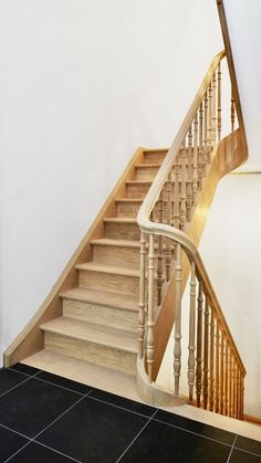 a wooden stair case next to a white wall and black tile floor in a house