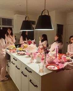 a group of women in pink robes standing around a kitchen counter with food on it