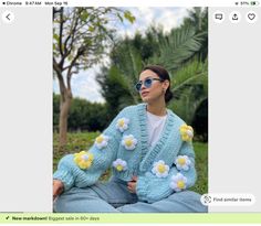 a woman sitting on the ground wearing a blue knitted cardigan with yellow and white flowers