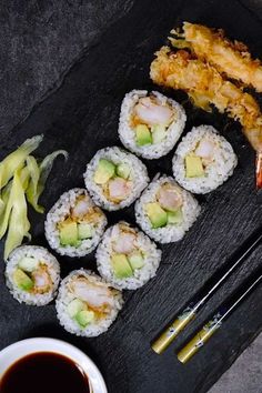 sushi with chopsticks and sauce on a black plate next to some vegetables