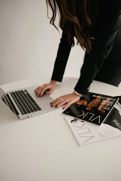 a woman bending over on top of a white table next to a laptop and magazine