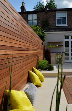 a wooden fence with pillows and plants in the foreground, next to a house