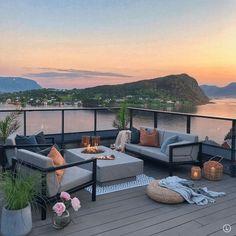 a deck with couches and tables on it overlooking the water at sunset or sunrise