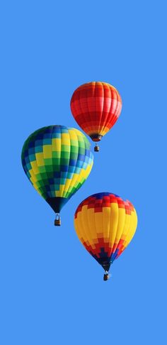 three colorful hot air balloons flying in the blue sky with no clouds on their sides