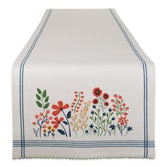 an embroidered table runner with flowers and leaves on the border, in white linens