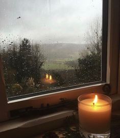 a candle sitting on top of a window sill in front of a rain soaked window