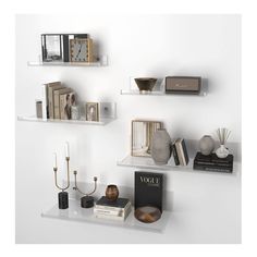 three white shelves with books, candles and other items on them against a white wall